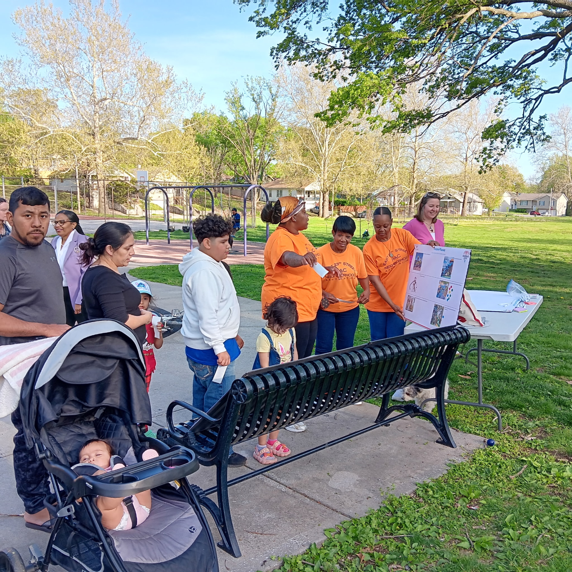 East 23rd Street PAC Neighborhood Association volunteers in orange shirts sharing resources with families at a neighborhood park.