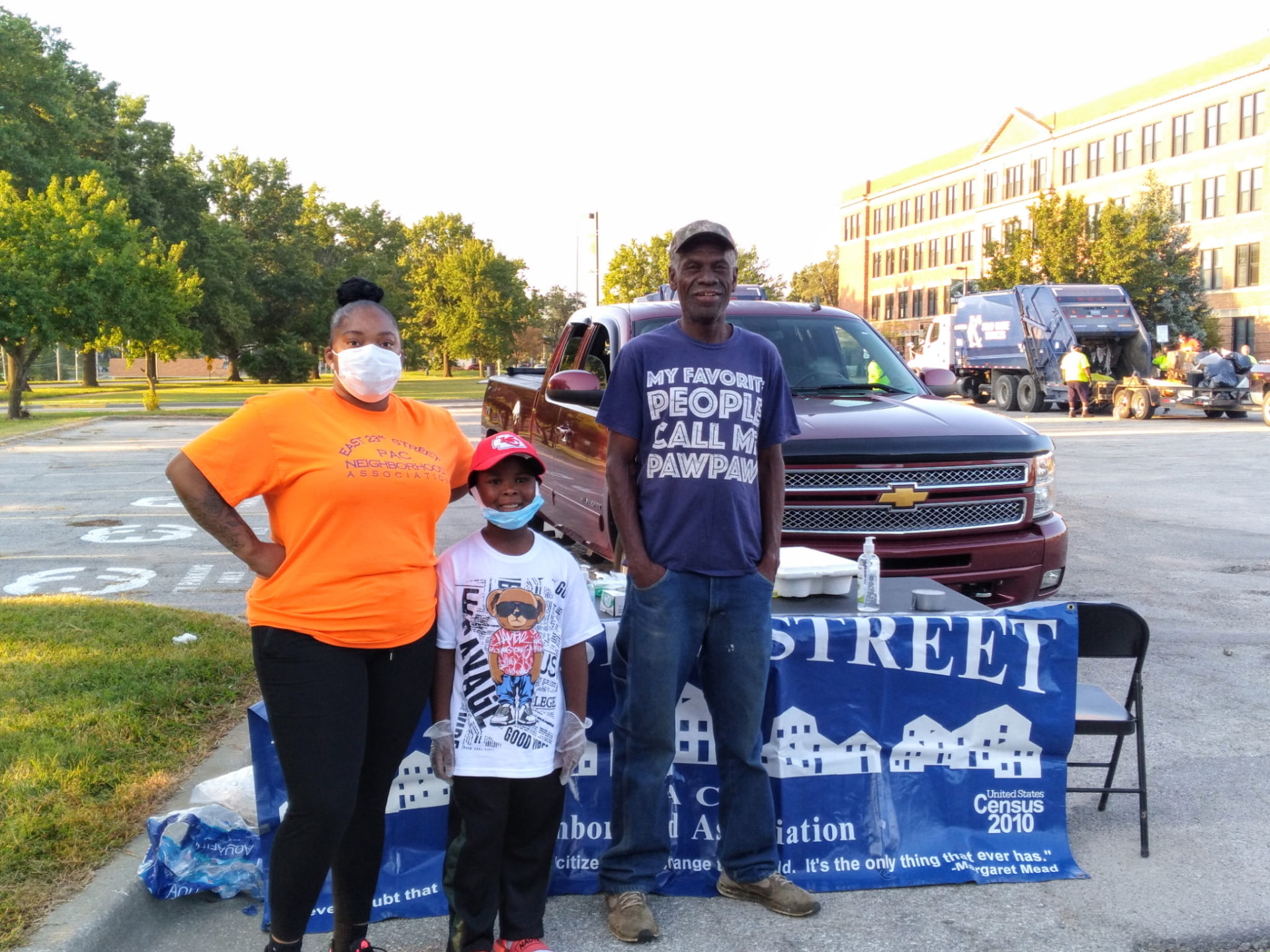 Sharlonda Riley in an East 23rd Street PAC shirt with a family at a community resource event in front of a neighborhood association banner.